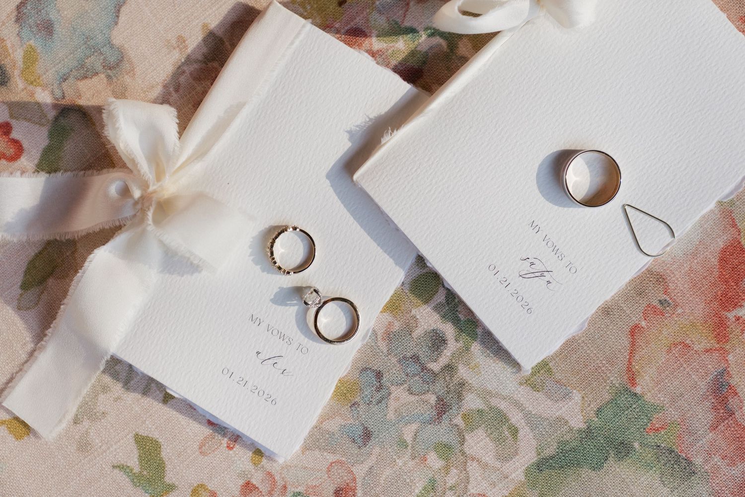 Elegant wedding flat lay with gold hoop earrings, a ring, and white ribbon-tied gift boxes on floral background.