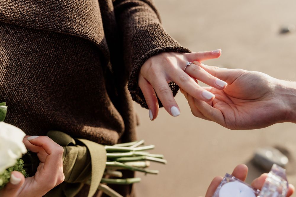 Close-up of a romantic marriage proposal with a ring being placed on a woman's finger at the beach.