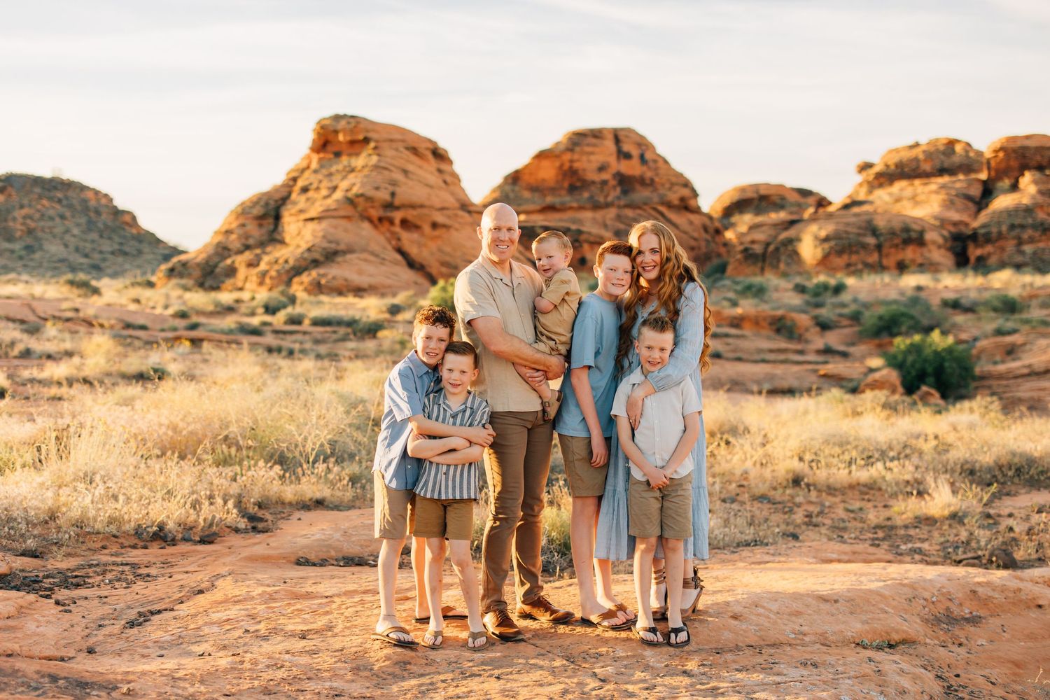 Family of seven posing together in a scenic desert landscape with red rock formations at golden hour.