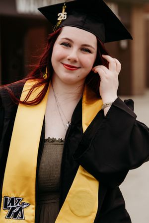 Smiling graduate with red hair wearing black cap and gold WK stole poses for senior portrait.