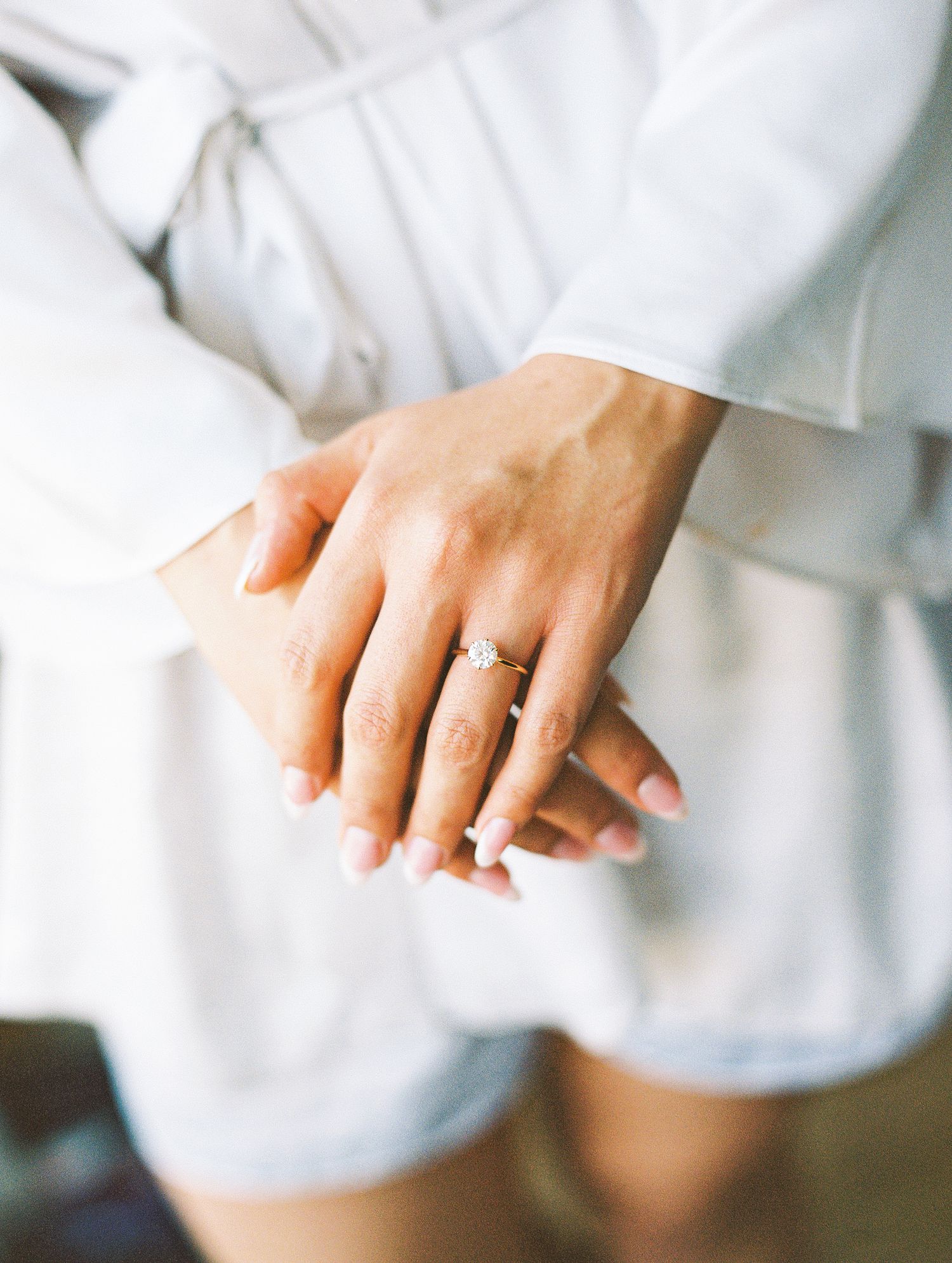 Close-up of hands with elegant diamond engagement ring and French manicure, wearing white wedding day robe.