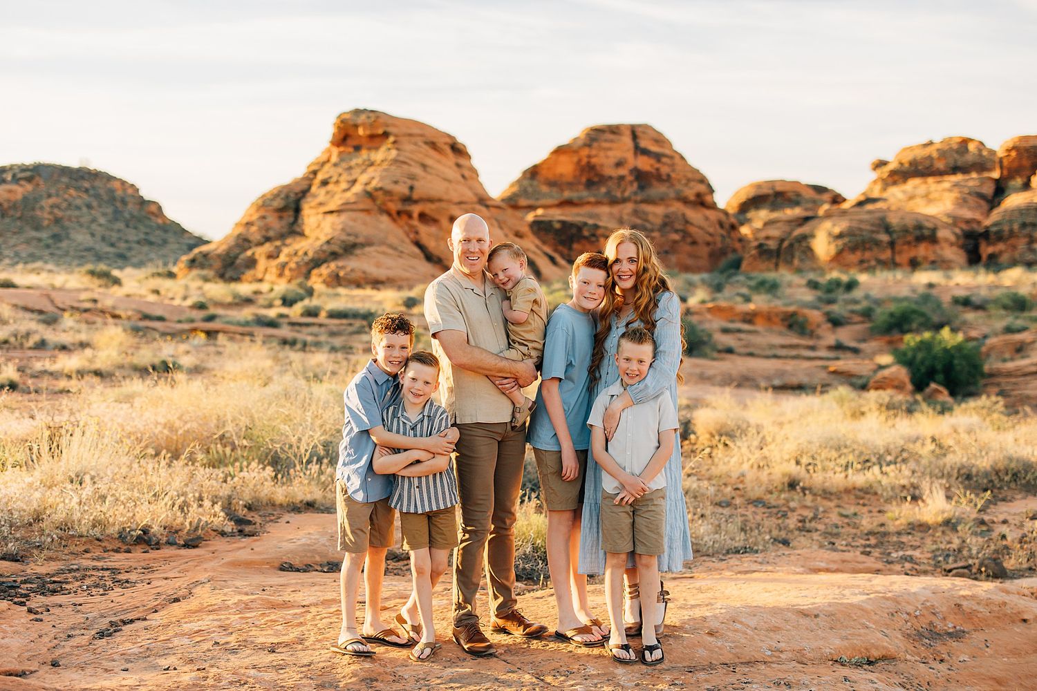 Family of six posing together in a red rock desert landscape during golden hour photography session.