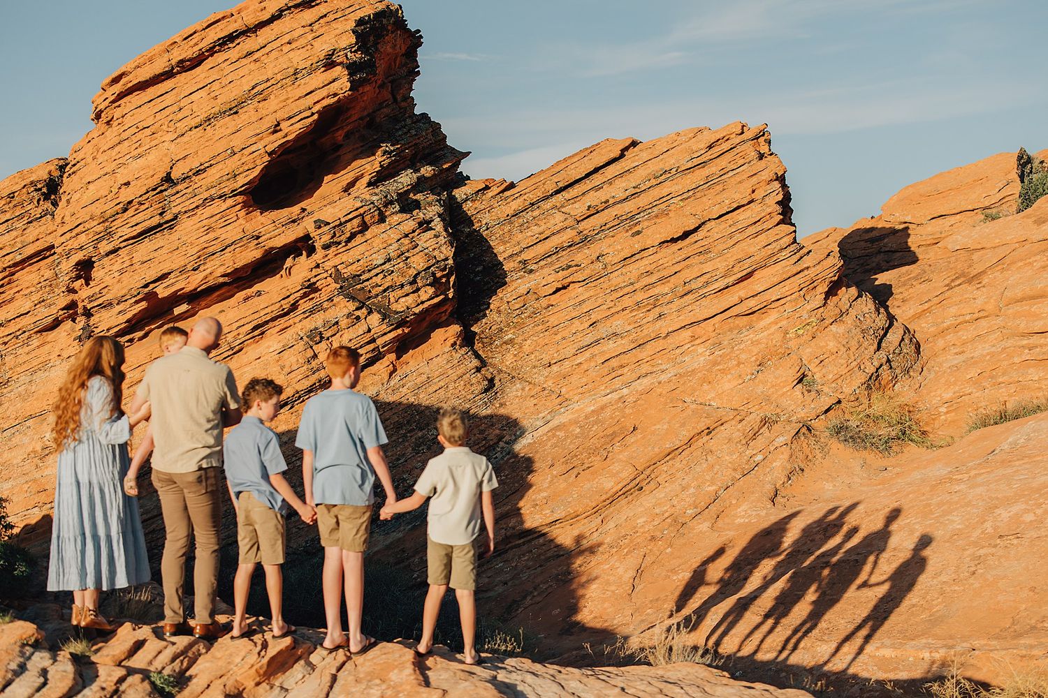 Family holding hands facing red rock formations at Red Rocks Park, Colorado, on a sunny day.