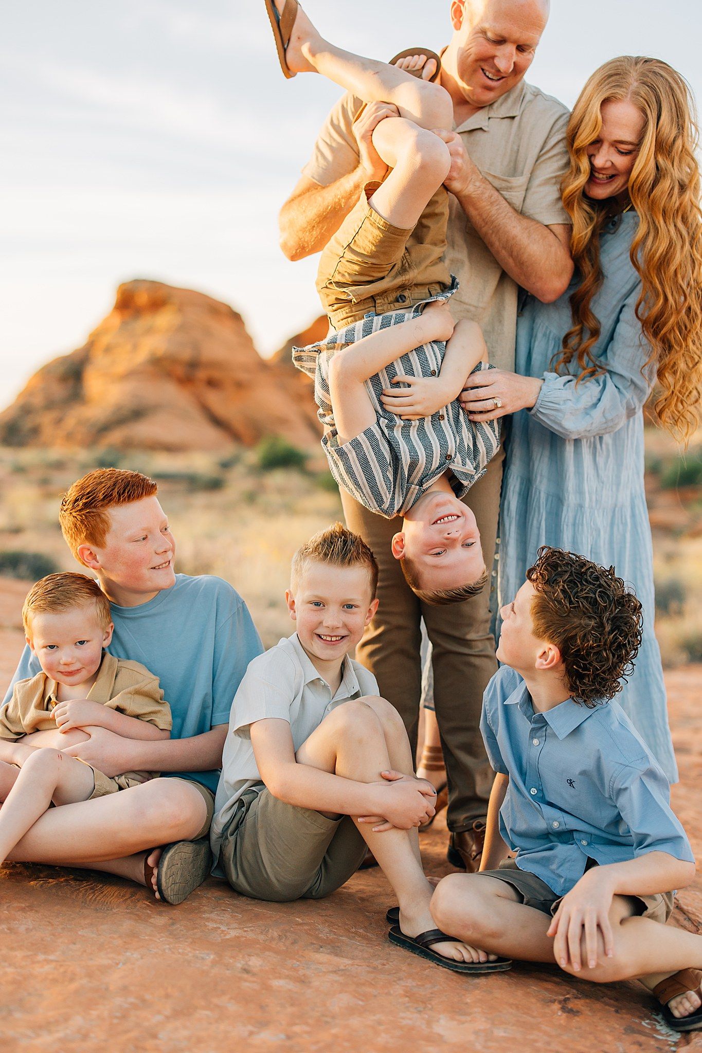Large family with five boys and parents laughing outdoors at a red rock desert location.