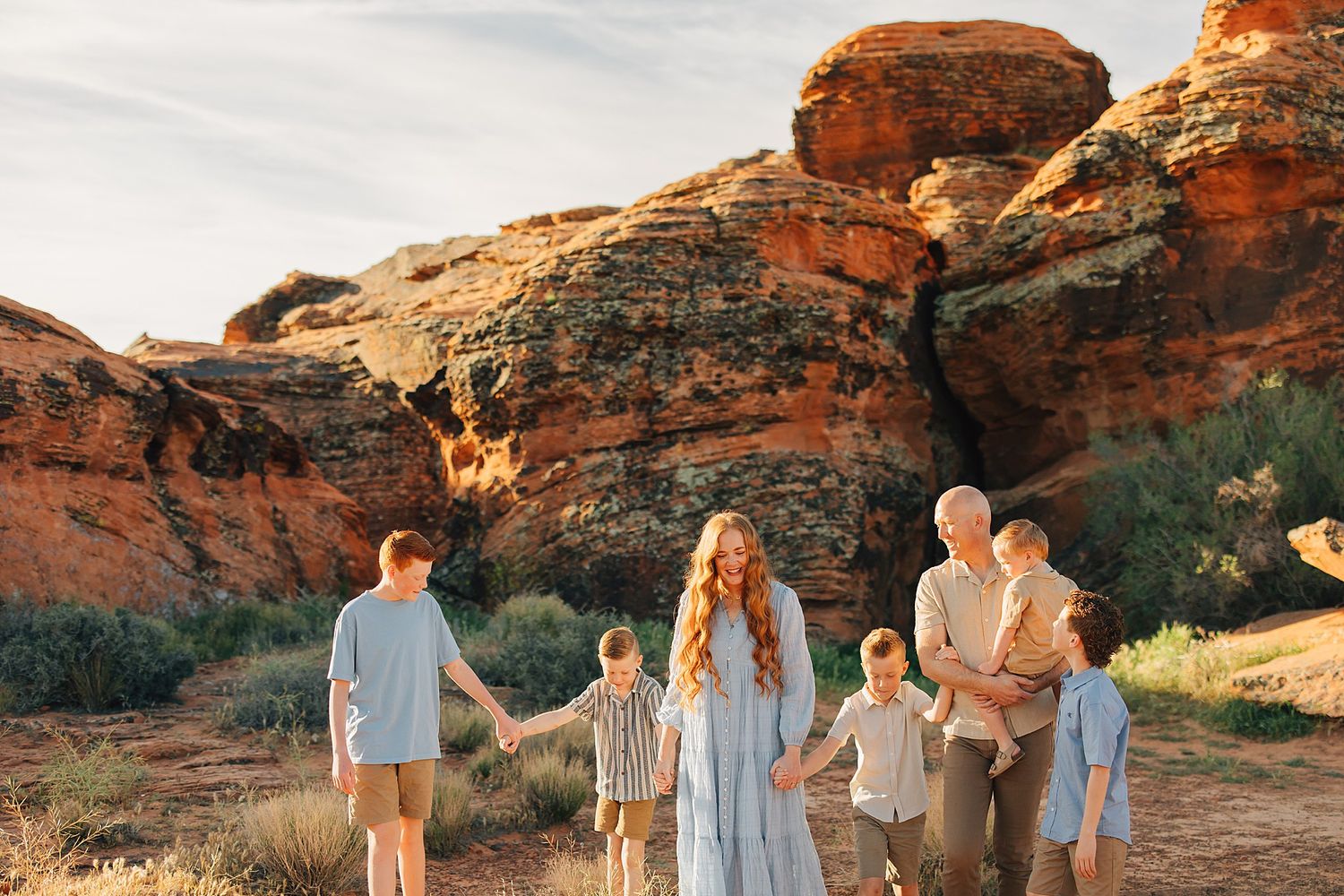 Family of six walking together among red sandstone rocks in warm golden sunset light.