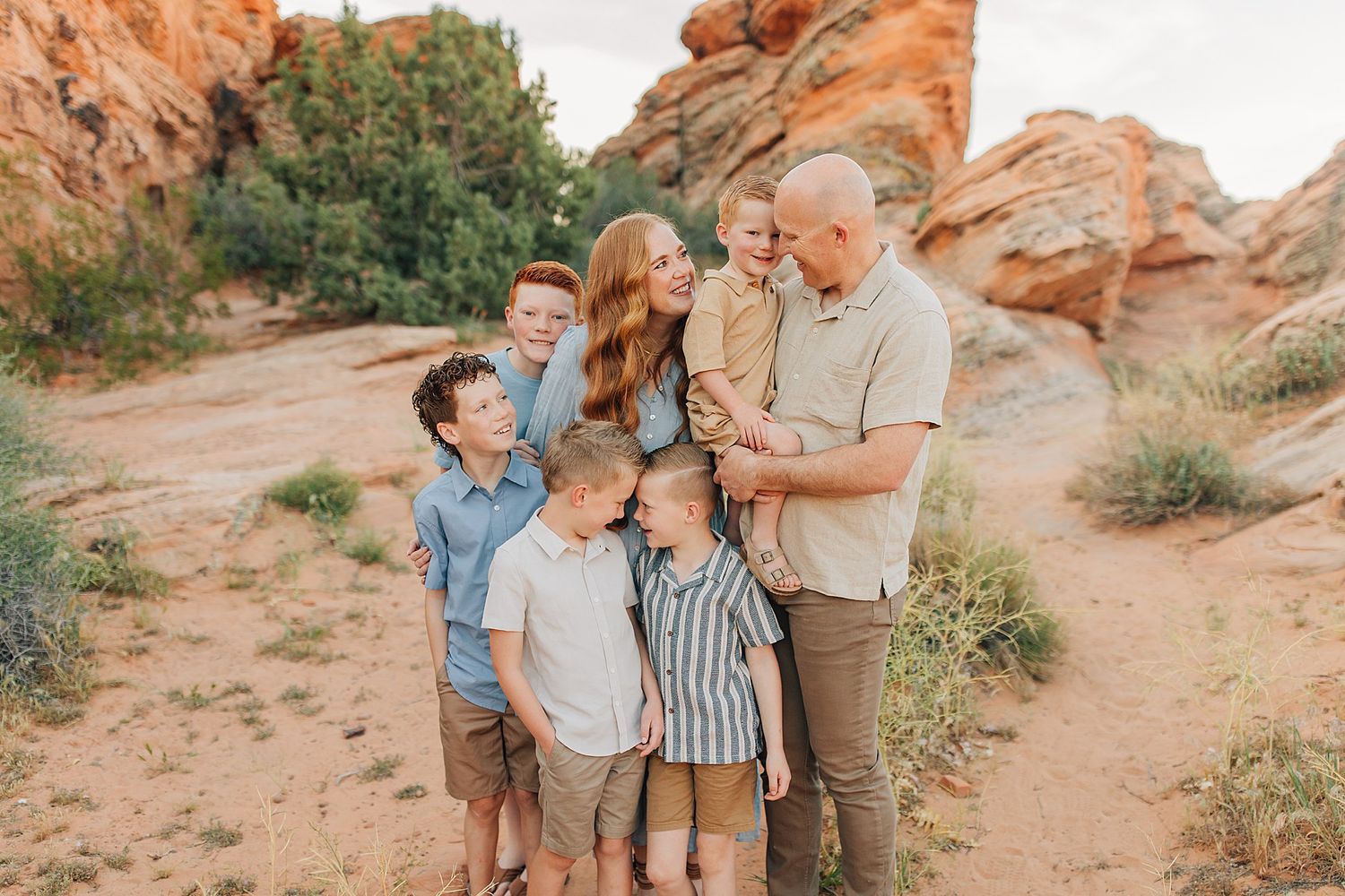 Family of six poses together among red rock formations in a desert landscape during a warm outdoor photo session.
