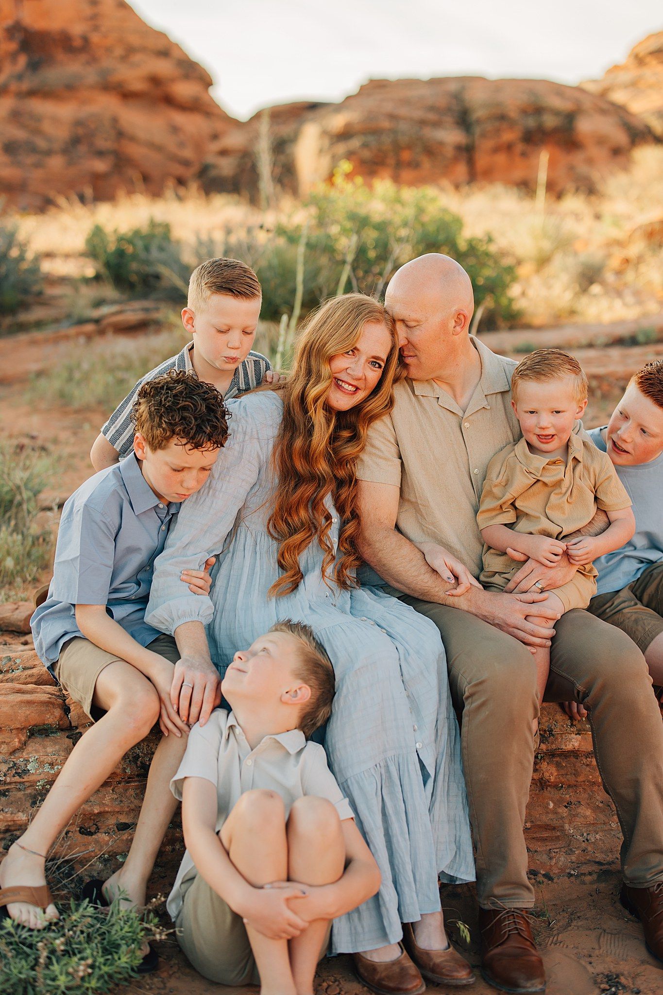 Happy family of six sits together on rocks in a scenic desert landscape.