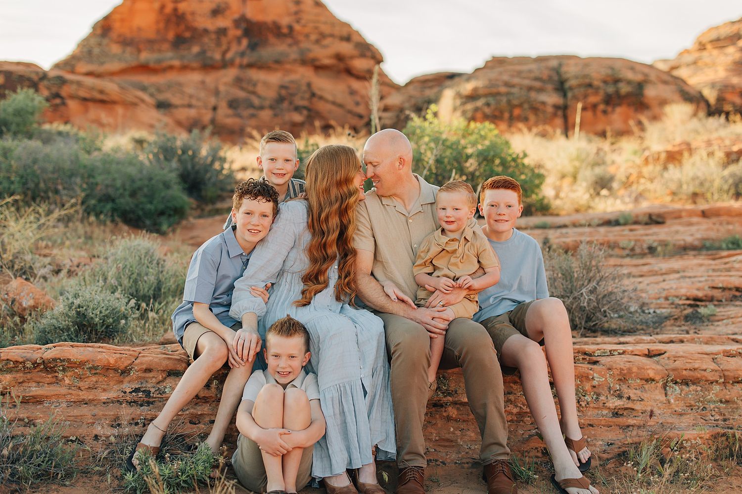 Family of six poses on red rocks in a desert landscape at golden hour.