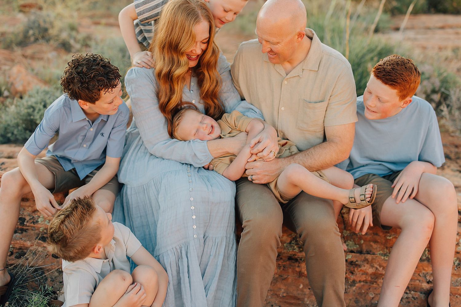 Family of six with parents and four children sharing a tender moment outdoors in a desert landscape during a photo session.