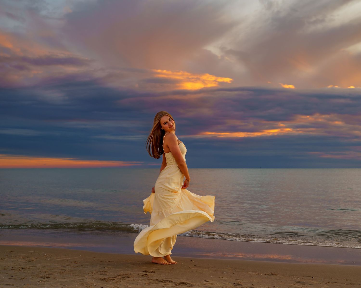 Young woman with auburn hair embracing herself on a beach at golden sunset, eyes closed peacefully.