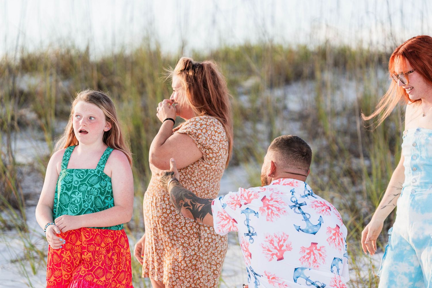 Family of four enjoying a sunny beach day near sand dunes, wearing colorful summer outfits.