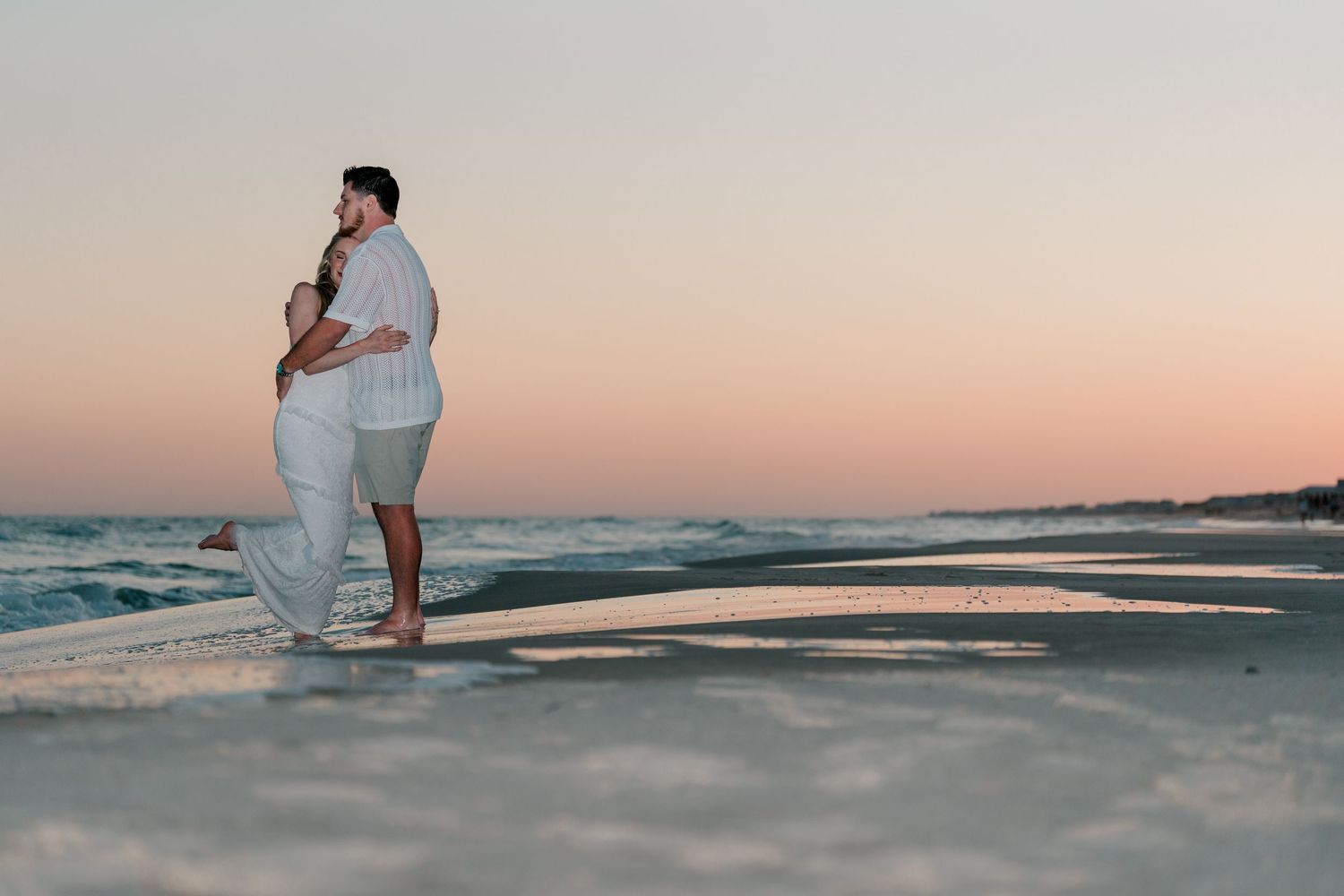 Romantic couple hugging barefoot on the beach during a breathtaking pink and purple sunset.