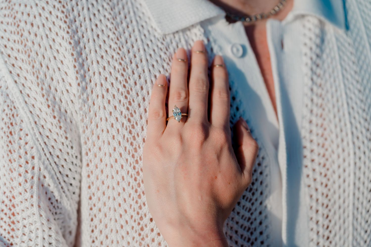Close-up of a woman's hand displaying a stunning engagement ring while resting on a white knit sweater.