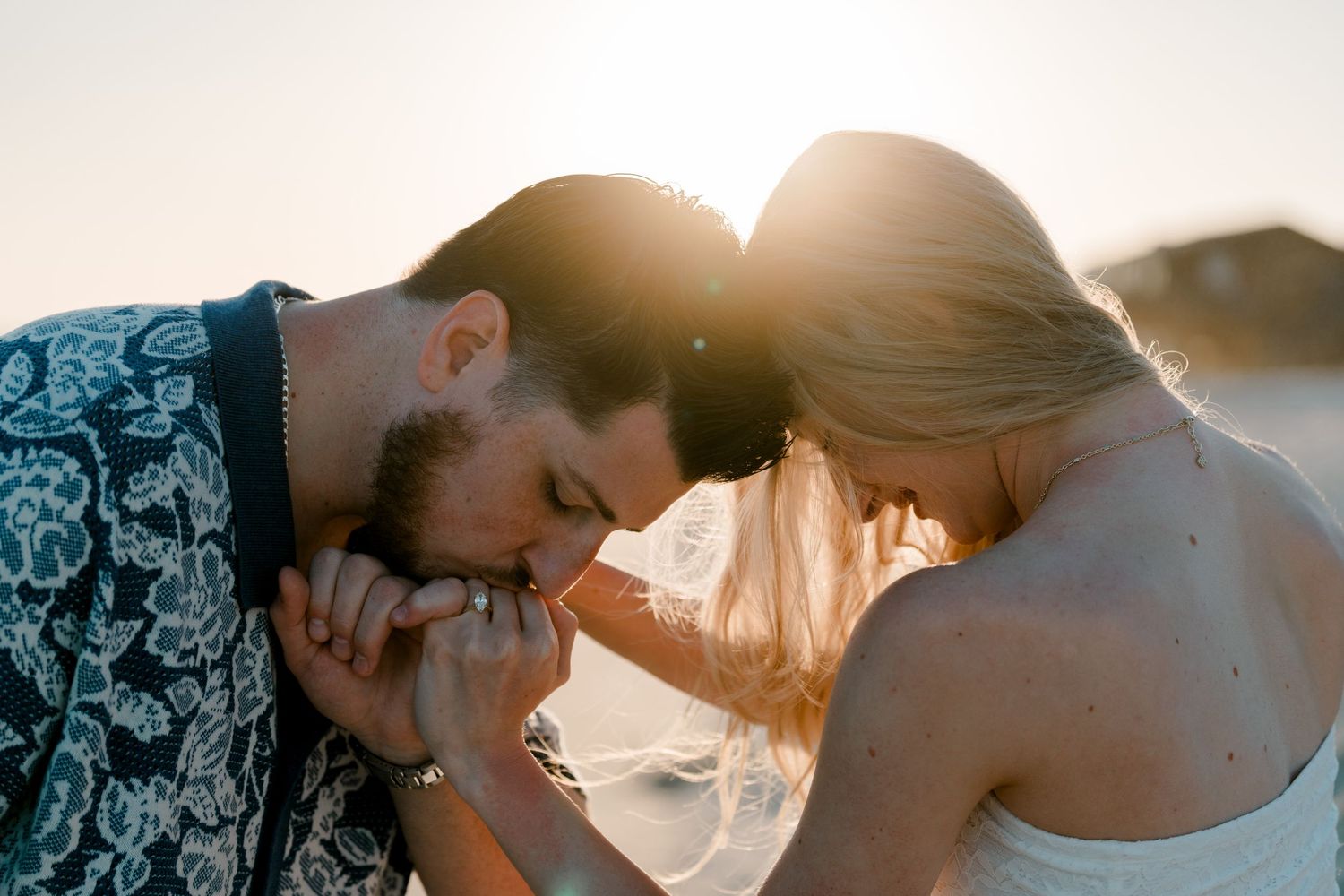 Couple sharing a romantic sunset kiss, man gently holding woman's hand in golden backlight.