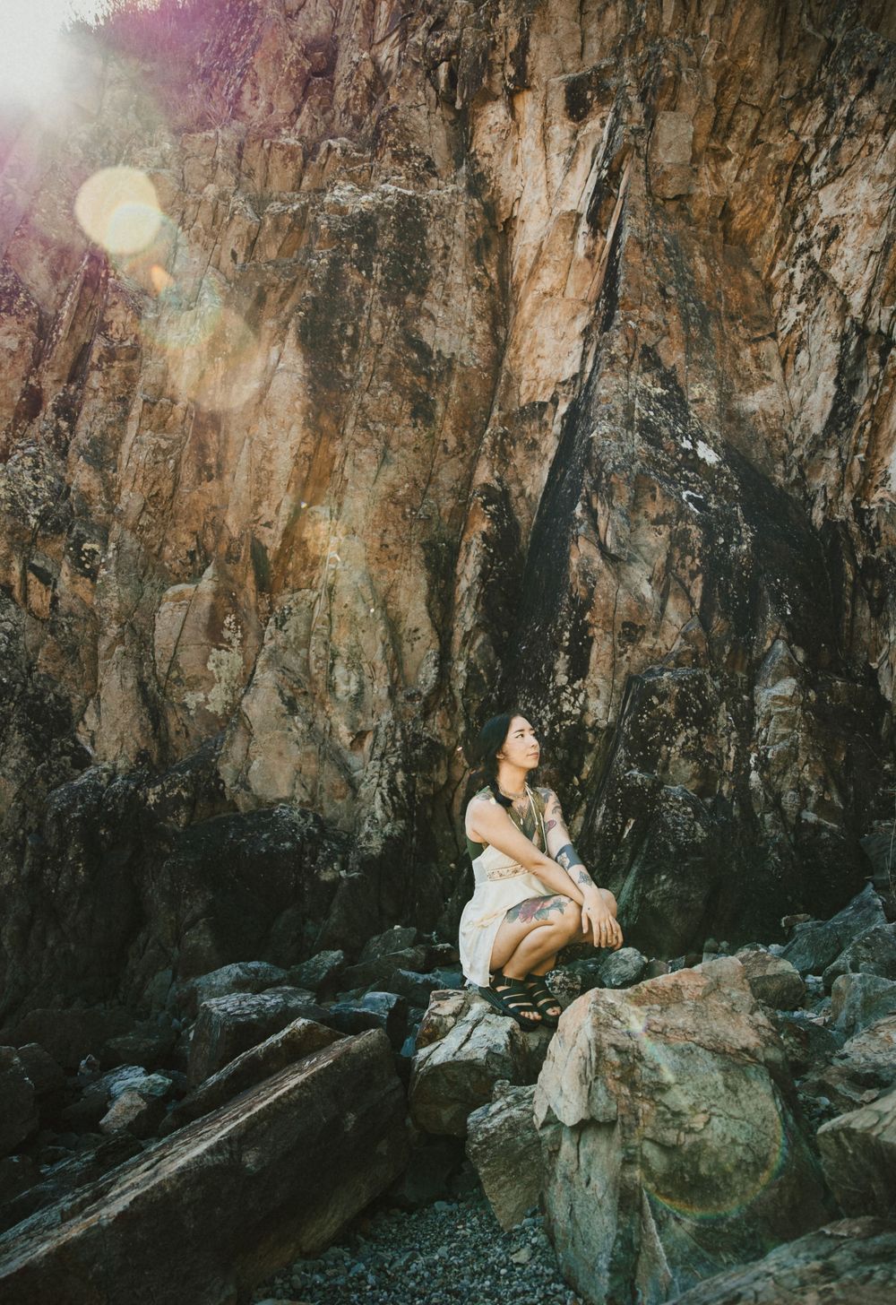 Woman in white dress sitting on rocky cliff face, bathed in golden sunlight streaming from above.
