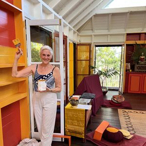 Woman holding paint brush and can in colorful orange and red bohemian style tropical home interior.