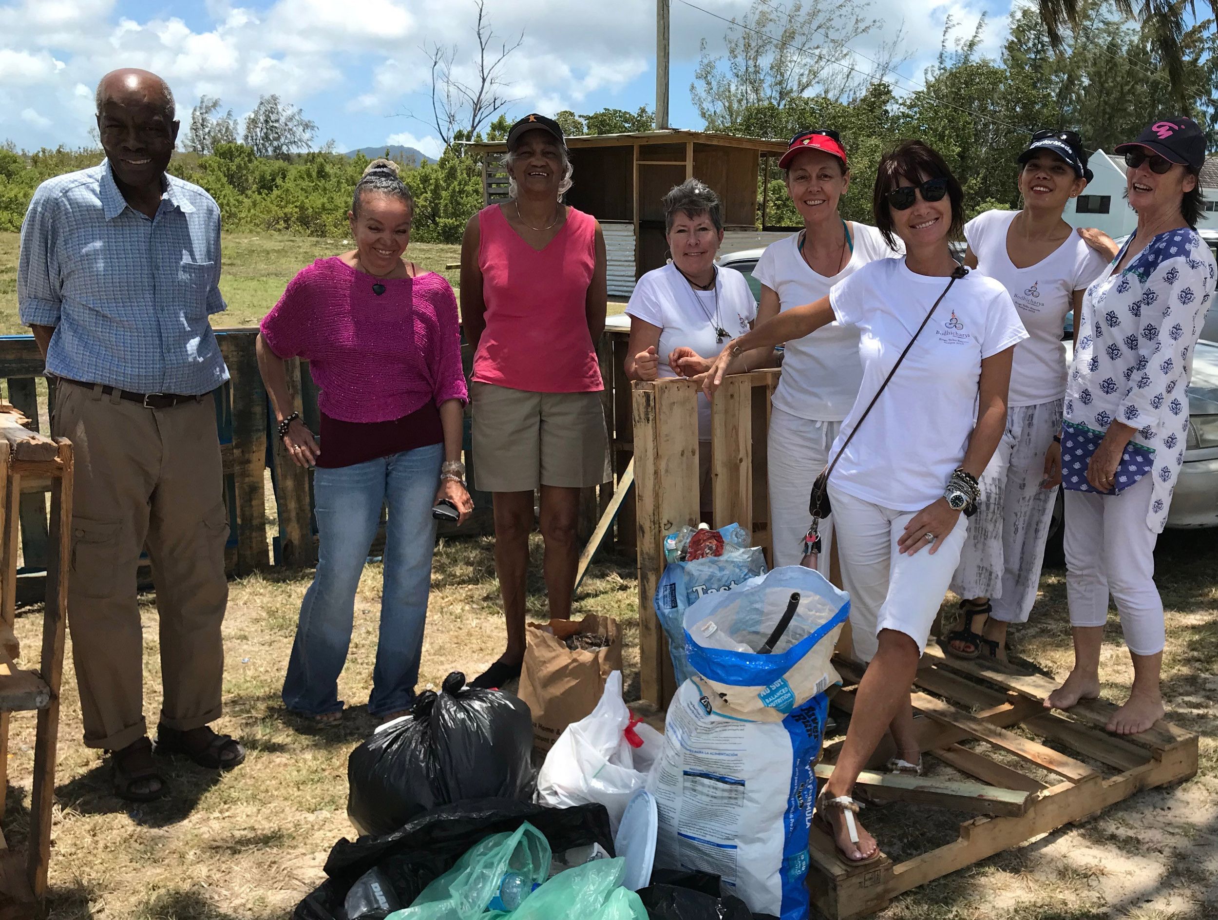 Group of volunteers posing outdoors with collected garbage bags and recycling materials during a community cleanup event.