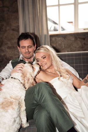 Bride and groom relaxing on a sofa with their fluffy dog on their wedding day.