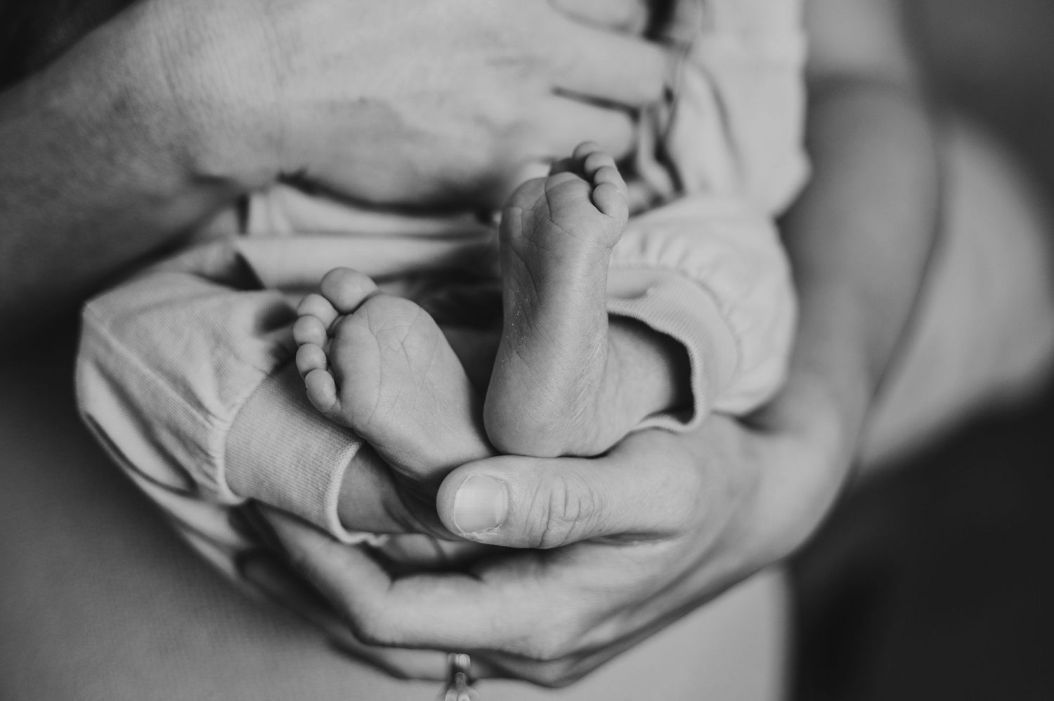 A mother holds newborn baby and holds his bare feet up in her hands.