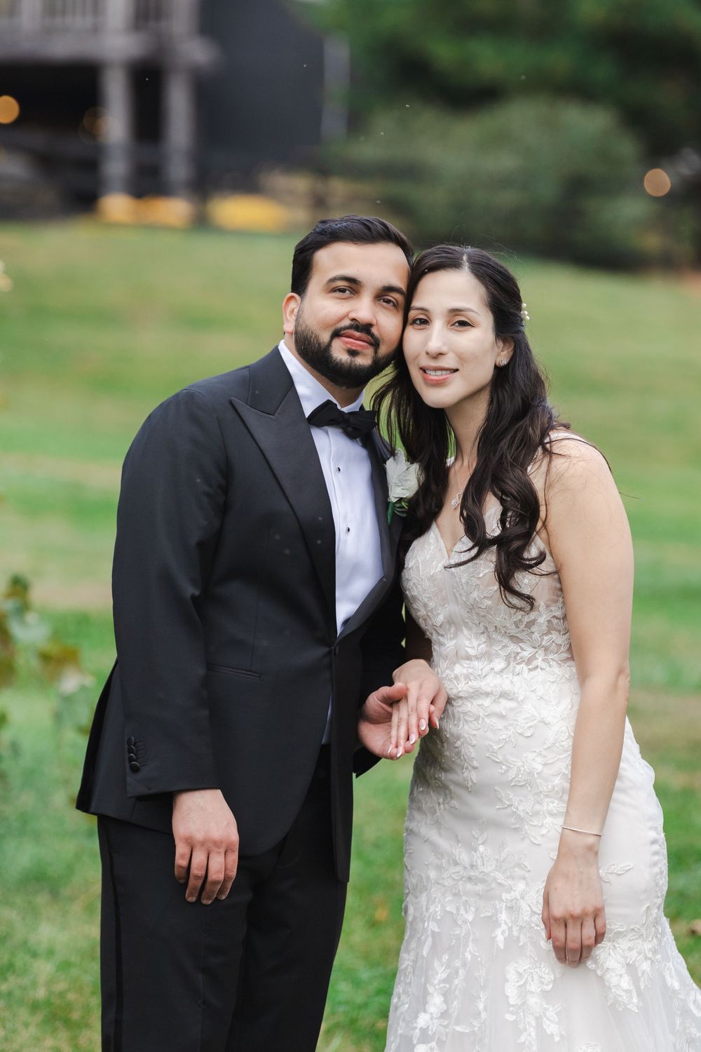 Bride and groom pose together smiling on green lawn at outdoor wedding.