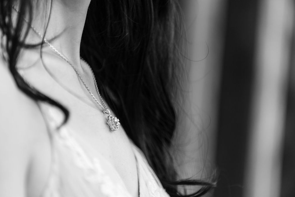 Black and white close-up of a woman wearing a delicate silver pendant necklace with dark flowing hair.