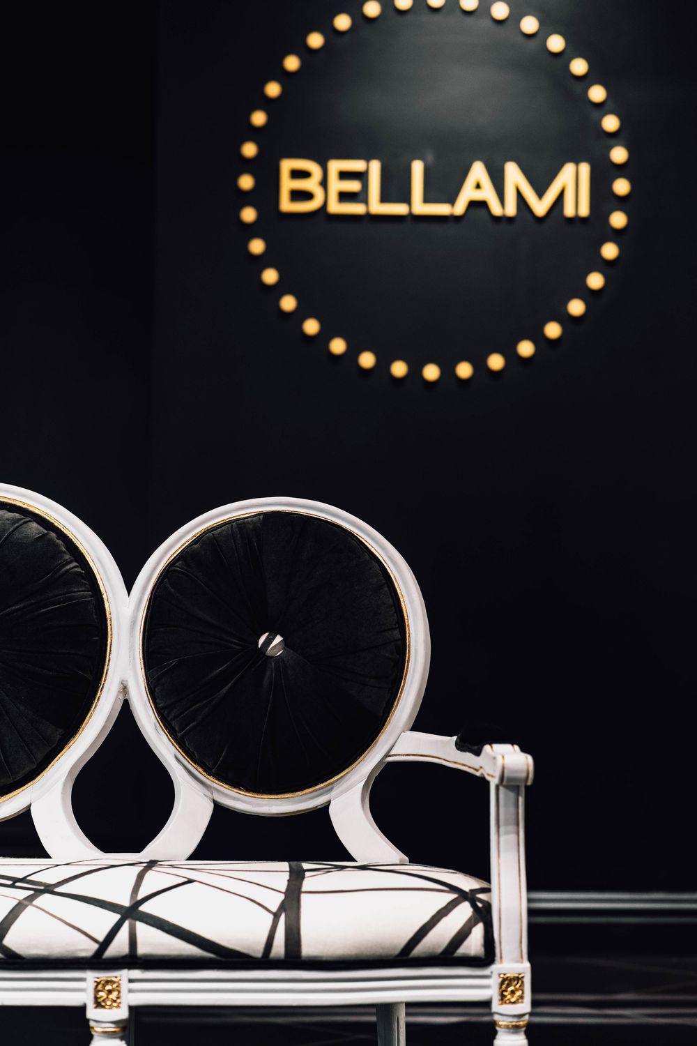 Elegant white and black chair in front of illuminated Bellami logo sign on dark wall.