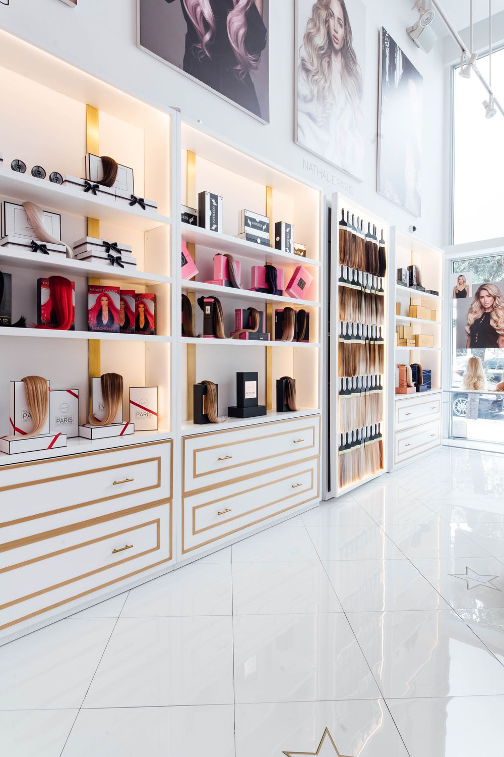 Elegant white and gold hair salon shelving displaying extensions, styling tools, and beauty products in a luxury boutique.