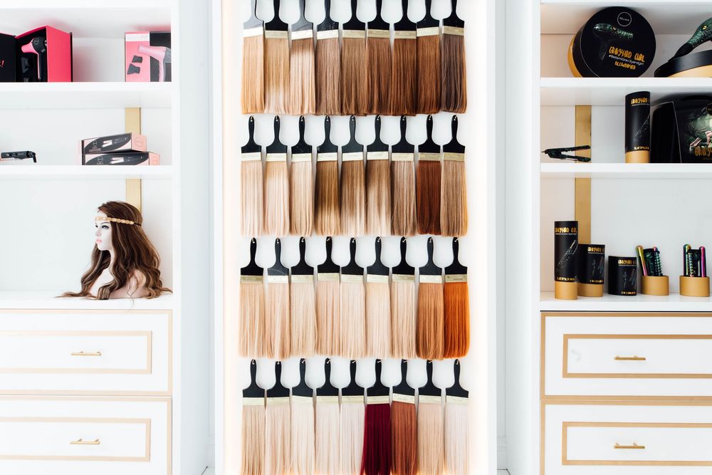 Wall display of hair extension color swatches ranging from blonde to brunette shades in a bright white salon.