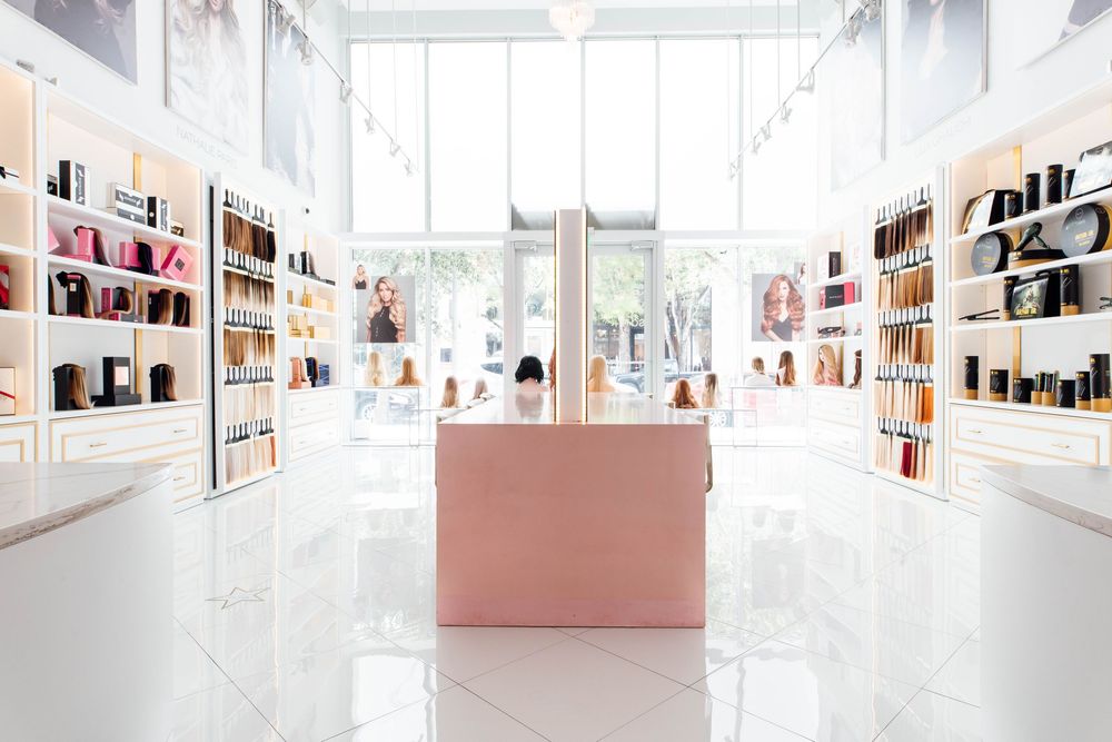 Bright modern beauty store interior with white shelves displaying cosmetics and a pink reception desk on glossy white floors.