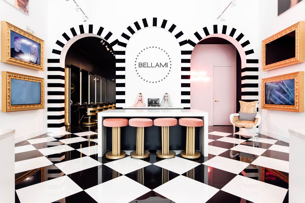 BELLAMI salon reception area with black and white checkered floors, pink accents, and bold striped archways.