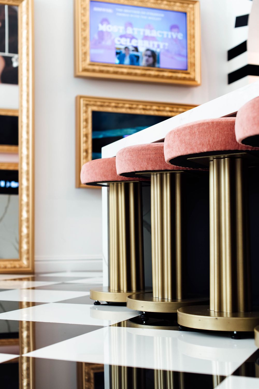 Pink velvet stools with gold bases on a black and white checkered floor in a stylish salon waiting area.