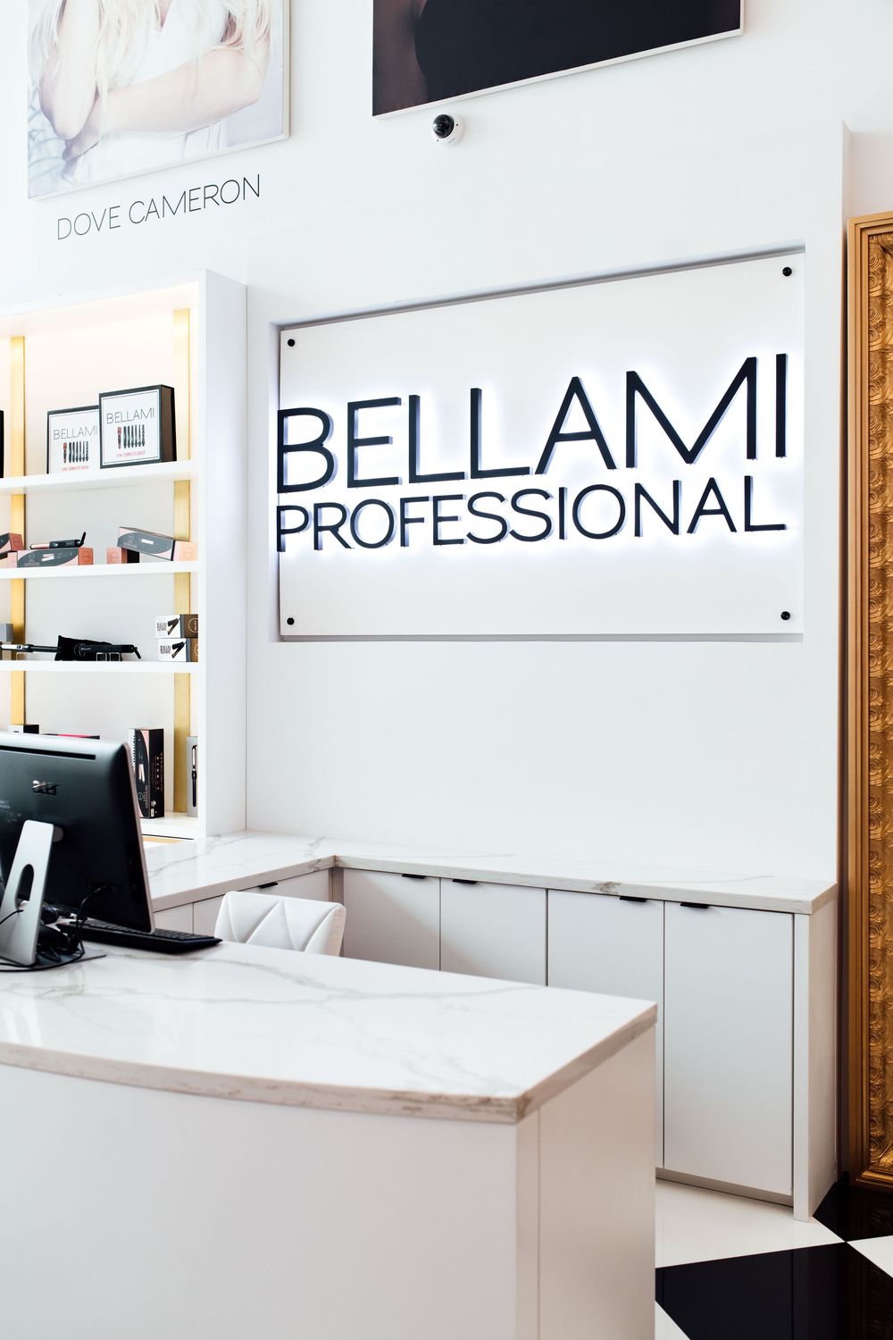 Bellami Professional salon reception desk with illuminated sign and modern white interior design.
