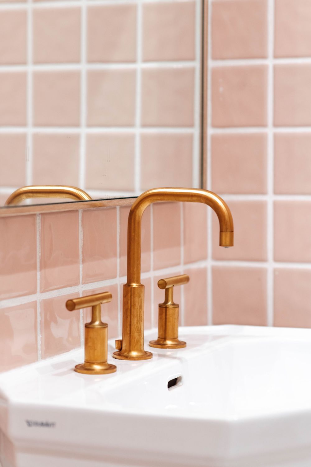 Luxury brass three-hole faucet on white sink with pink ceramic tile wall in modern salon bathroom.