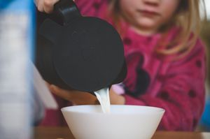 Child pouring milk from a black pitcher into a white bowl, baking preparation activity.