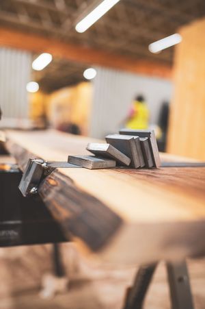 Metal clamps and blocks resting on a rustic live-edge wooden workbench in a carpentry workshop.