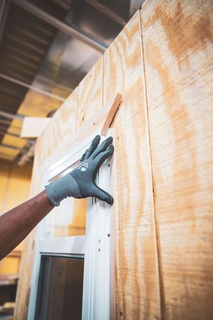 Worker wearing gray gloves installing plywood panels on a wall frame during interior construction.