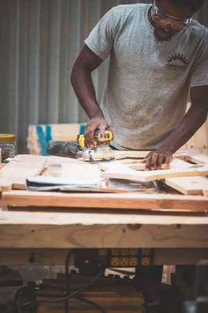 Skilled woodworker using a power router to shape lumber on a workbench in a carpentry workshop.