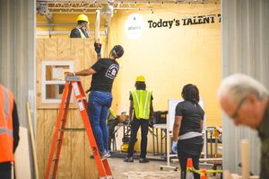 Construction students building a wooden structure indoors at a vocational training facility with ladders and tools.