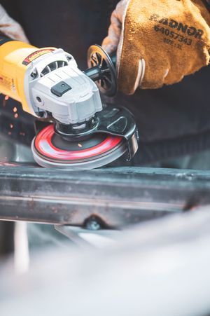Worker using a yellow angle grinder on metal with leather safety gloves, sparks flying in a workshop.