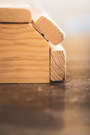 Close-up of wooden building blocks arranged as a miniature house on a reflective surface with warm bokeh background.