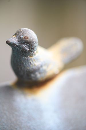Close-up of a rustic blue ceramic bird figurine with vintage patina, sitting on a gray surface.