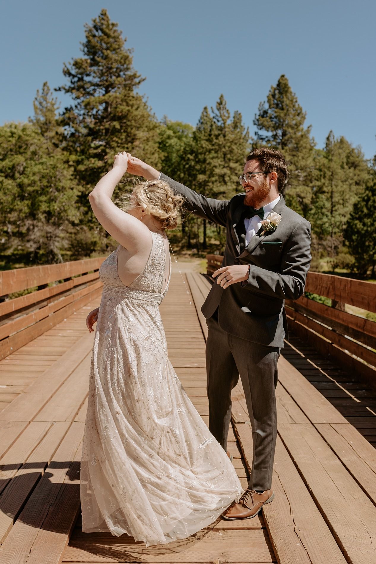 Bride and groom dancing on a wooden bridge surrounded by pine trees on their wedding day at Lake Cuyamaca, Julian.
