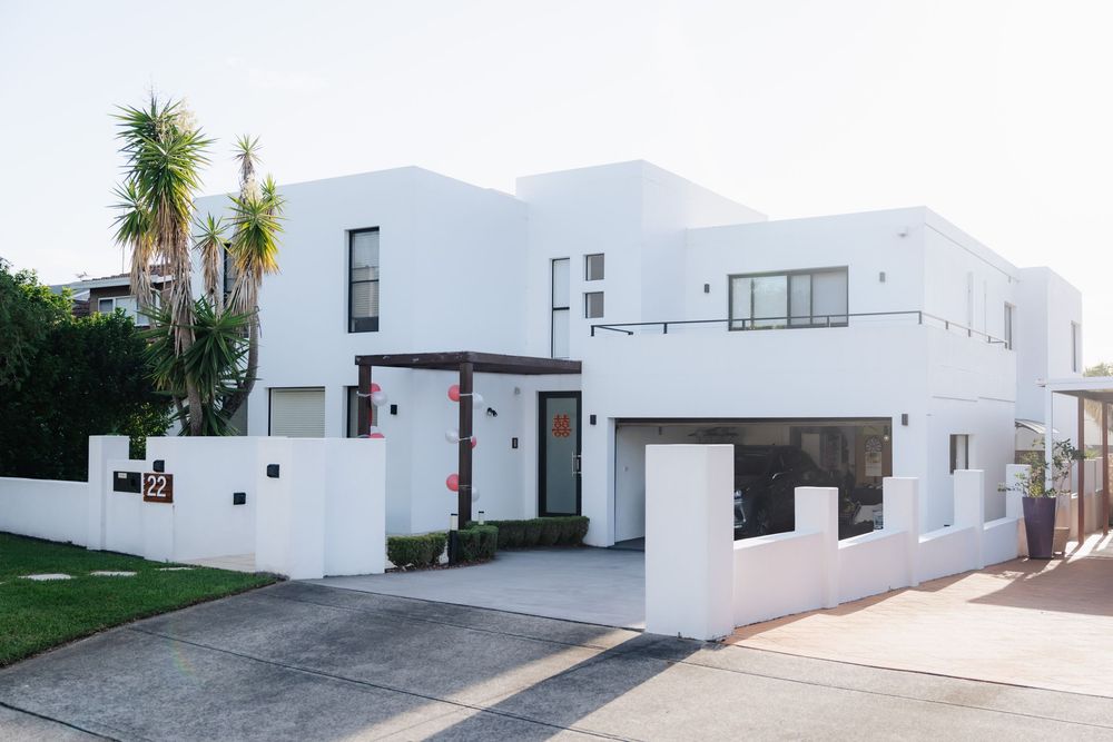 Modern white two-story home with flat roof, palm trees, and a private driveway in a sunny coastal neighborhood.