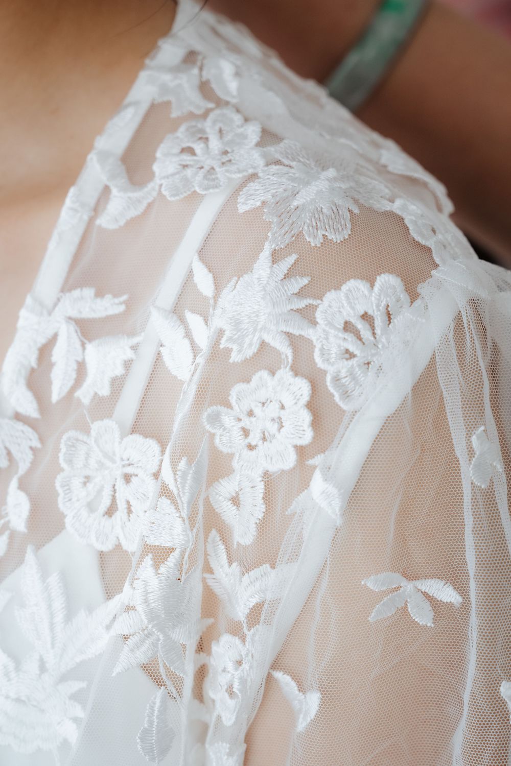Close-up of elegant white floral lace wedding dress fabric with intricate embroidered flower details on sheer tulle.