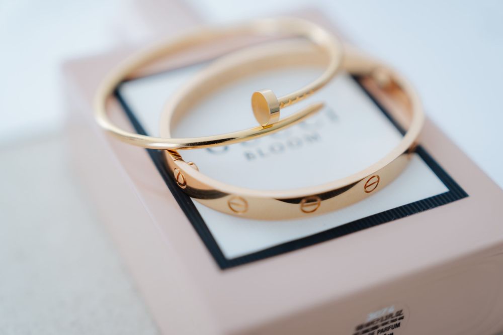 Elegant gold Cartier Love bracelet and nail bangle displayed on a pink luxury gift box.
