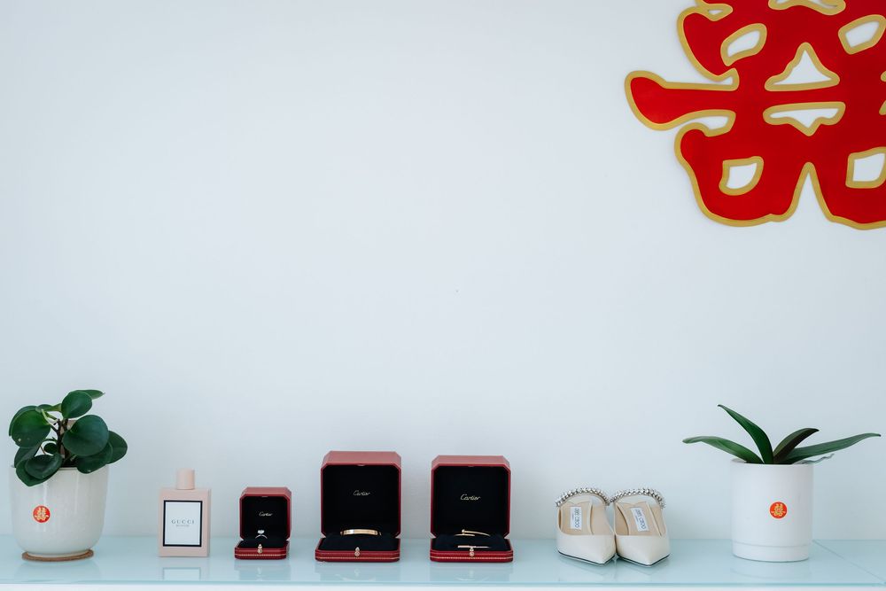 Red jewelry boxes with rings and accessories displayed on a white shelf with plants and a Chinese double happiness symbol.