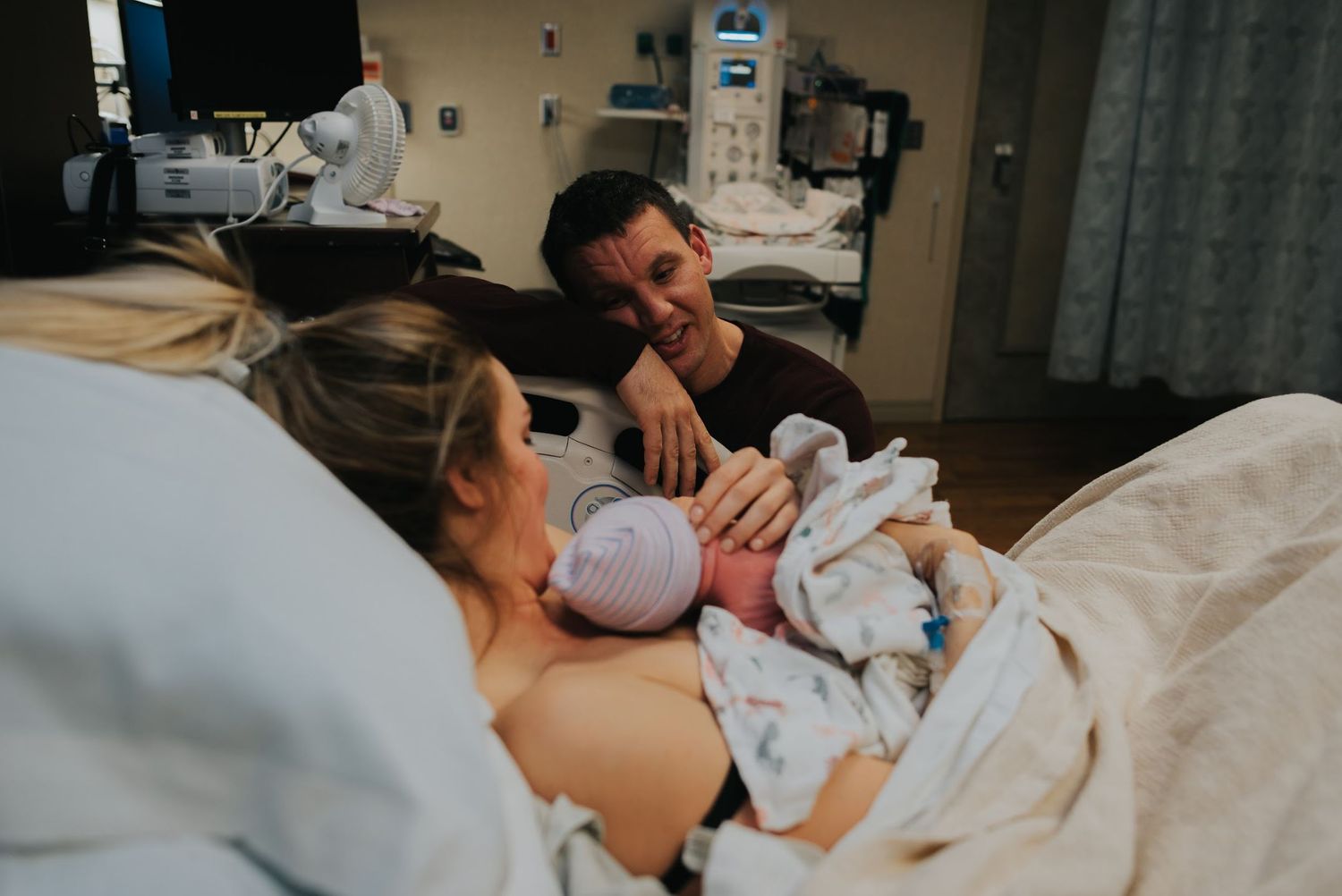 New parents share an intimate moment with their newborn baby in a hospital room.