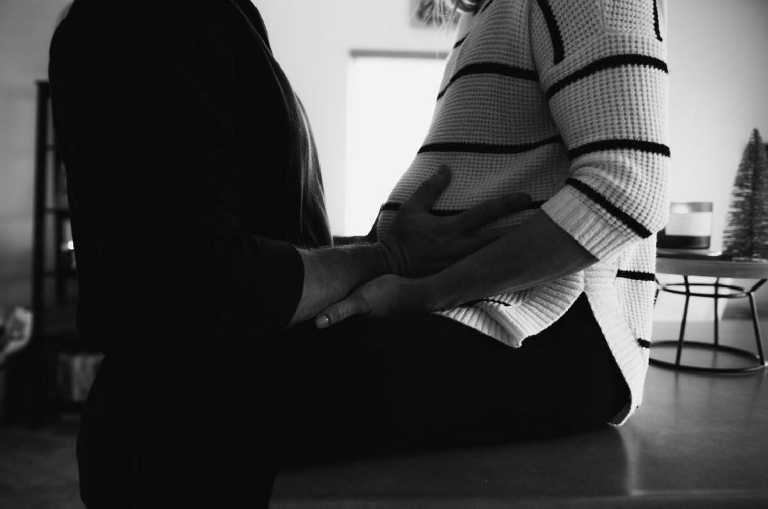 Close-up black and white photo showing hands resting on knees in casual indoor setting.