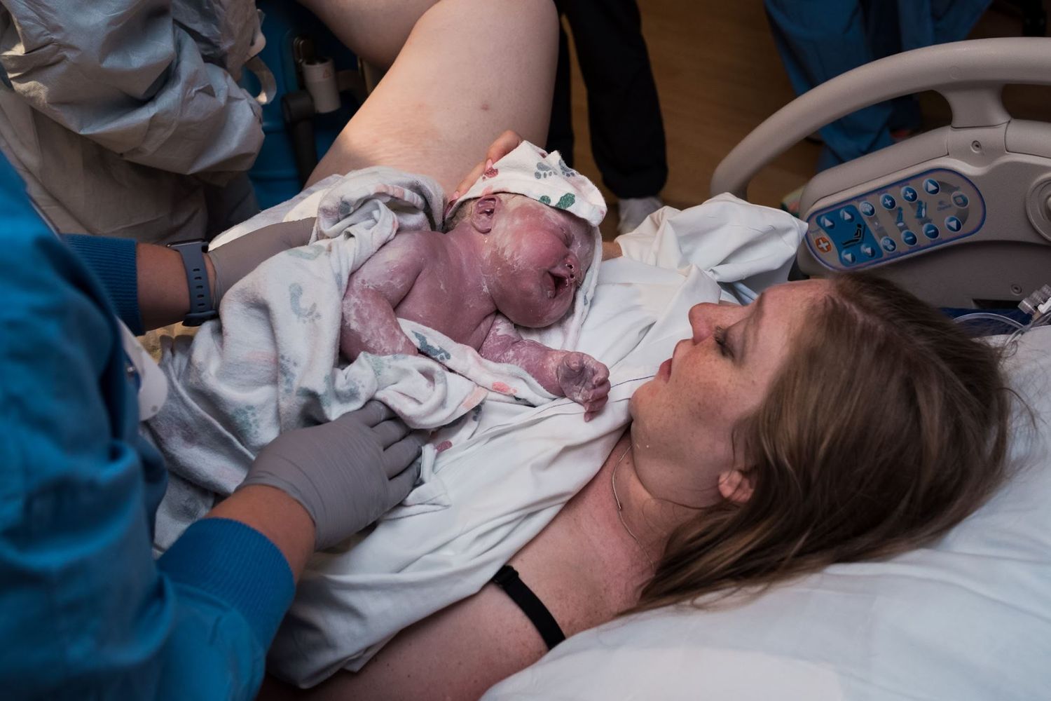Newborn baby placed on mother's chest immediately after birth in hospital delivery room.