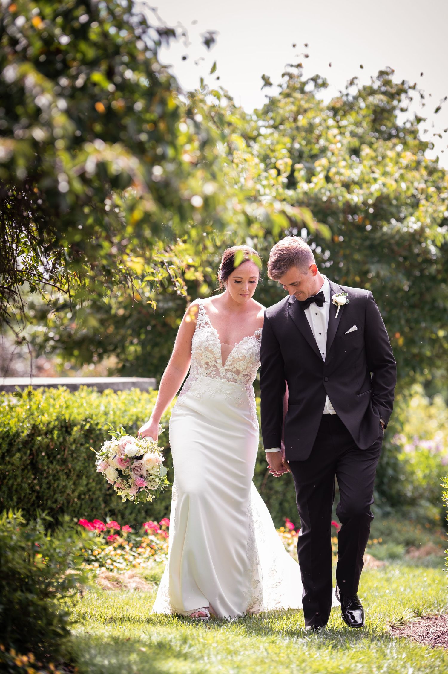 Bride and groom walking hand in hand through lush green garden on their wedding day.